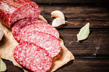 Pieces of salami sausage with garlic and bay leaf on paper. 