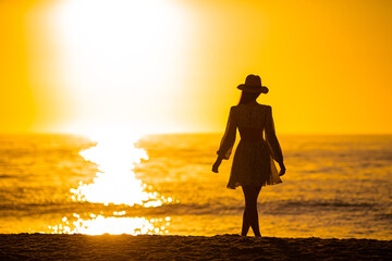 Young beautiful woman at straw hat on the beach at sunset