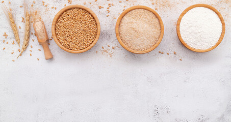  Wheat grains , brown wheat flour and white wheat flour in wooden bowl set up on white concrete background. - 564098971