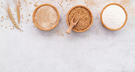  Wheat grains , brown wheat flour and white wheat flour in wooden bowl set up on white concrete background.