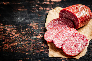 Sliced salami sausage on paper on the table.