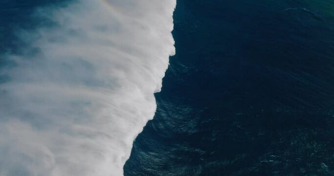 Slow motion aerial view of giant blue ocean wave crashing
