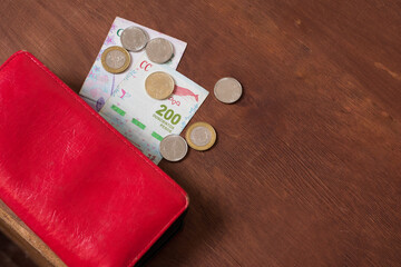 billetes y monedas de pesos argentinos con una cartera roja sobre un fondo de madera marron
