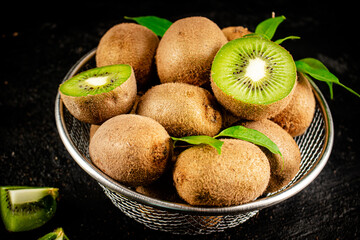 Ripe kiwi with leaves in a colander on the table. 