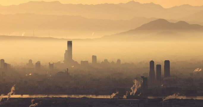 Factory emissions mix with thick layer of smog over city at sunrise