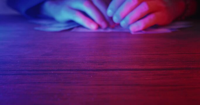 Close up lucky male winner hands grabbing bunch of dollars lying on casino table in neon light. Happy winner received winnings money at casino. Man win cash money in gambling or lottery. Easy money