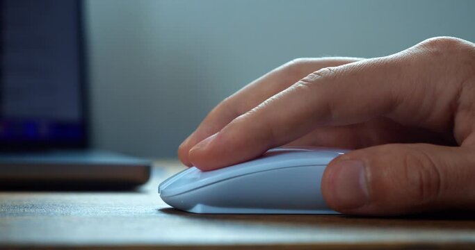 Clicking white computer mouse on a work desk. Human hand holding using mice for working online. Working with laptop computer using wireless handheld pointing device