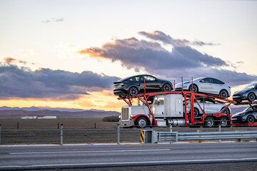 Powerful white big rig car hauler semi truck transporting cars on two level hydraulic semi trailer...