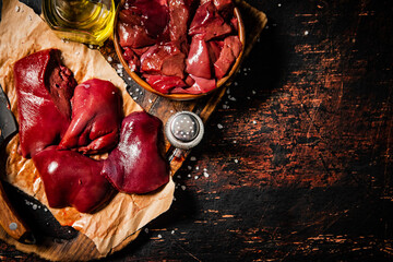 Pieces of raw liver on a cutting board with oil and spices. 