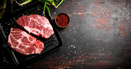 Raw pork steak in a frying pan with green onions and spices. 