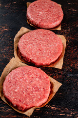 Raw burger on paper. On a rustic dark background.