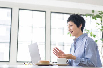 ノートパソコンを使ってテレビ電話で画面越しの相手と話をするアジア人女性、ミドル世代