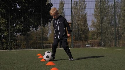 Soccer training for kids on the soccer field, a little boy trains in dribbling between orange cones.