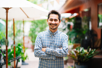 Portrait Asian young cool trendy man in plaid shirt crosses his arms standing outside in cafe.