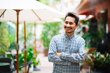 Portrait Asian young cool trendy man in plaid shirt crosses his arms standing outside in cafe.