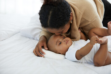 African young mother kissing her infant baby lying on the bed