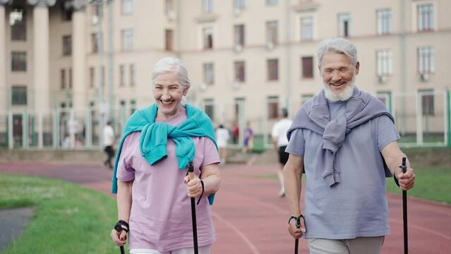 Two Elder Aged Adults Practicing Nordic Walking Park. European Senior Pensioner Couple With Trekking Sticks Hike Europe. Old Caucasian Grandparent Hikers Workout Arena. Healthy Love Smile Lifestyle.