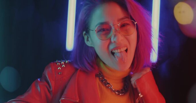 Portrait of cute Asian girl making funny faces and gesturing on beautiful black background with neon lights. Positive emotion and youth concept.