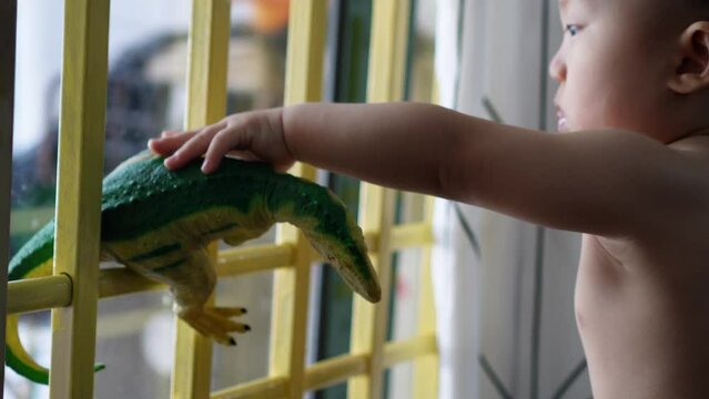 A naked baby boy plat Tyrannosaurus rex dinosaur toy near the door