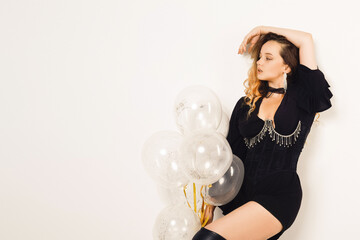 Gorgeous woman with balloons in black dress and corset with jewelry, long wavy hair posing on white background. Fashion , all black style.