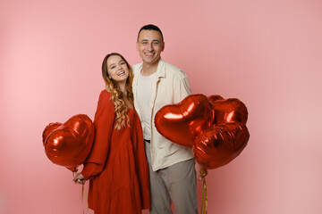 Couple, red balloons in the shape of a heart on a pink background. Valentine's Day, love, February 14. A woman in a red dress is smiling at the camera with a man.