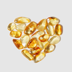 Amber stones on light background in shape heart transparent stone yellow beige color. Natural gemstone mineral material, healing crystal. Nature gems, top view Still life minimal style