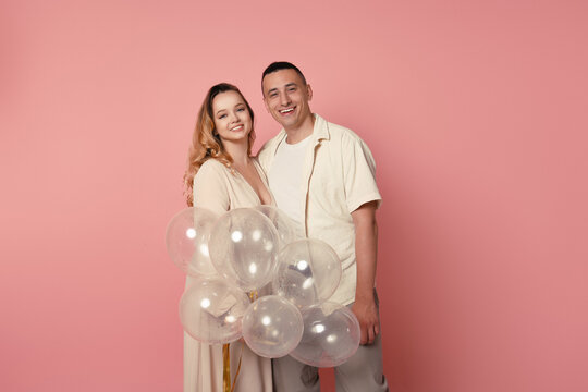 A young couple in pastel clothes, balloons on a pink background. Lovers celebrate and smile. A woman in a long dress, a romantic photo with a man, a date