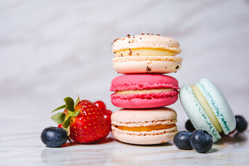 Obraz na płótnie Canvas Macaron pink, orange and beige, blue on marble style. A beautiful and beautiful French dessert. Fruits, Strawberries and lingonberries, blueberries, raspberries.