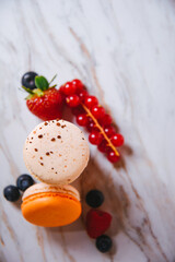 Macaron pink, orange and beige, blue on marble style. A beautiful and beautiful French dessert. Fruits, Strawberries and lingonberries, blueberries, raspberries.