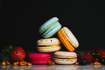 Colorful macarons cakes. Small French cakes. Sweet and colorful french macaroons. Many tasty macarons with fresh berries raspberries and blueberries, nuts on a black background.