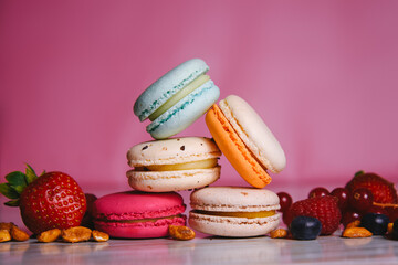 Colorful macarons. Small French cakes. Sweet and colorful french macaroons. Many tasty macarons with fresh berries, raspberries and blueberries, nuts and strawberries on a pink background.