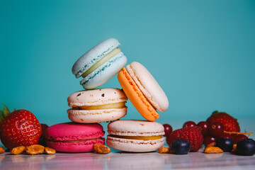 Colorful macarons. Small French cakes. Sweet and colorful french macaroons. Many tasty macarons with fresh berries, raspberries and blueberries, nuts and strawberries on a green background.