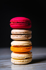 Macaron pink, orange and beige, blue on marble style and black background. French dessert on top of each other.