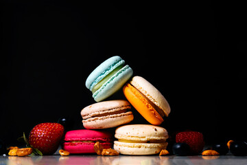 Colorful macarons cakes. Small French cakes. Sweet and colorful french macaroons. Many tasty macarons with fresh berries raspberries and blueberries, nuts on a black background