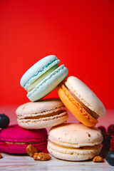 Colorful macarons. Small French cakes. Sweet and colorful french macaroons. Many tasty macarons with fresh berries, raspberries and blueberries, nuts and strawberries on a red background.