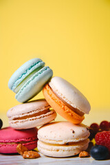 Colorful macarons. Small French cakes. Sweet and colorful french macaroons. Many tasty macarons with fresh berries, raspberries and blueberries, nuts and strawberries on a yellow background.