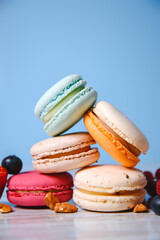 Colorful macarons. Small French cakes. Sweet and colorful french macaroons. Many tasty macarons with fresh berries, raspberries and blueberries, nuts and strawberries on a blue background..