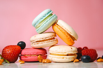 Colorful macarons. Small French cakes. Sweet and colorful french macaroons. Many tasty macarons with fresh berries, raspberries and blueberries, nuts and strawberries on a pink background.