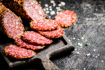 Sliced salami sausage on a cutting board with spices. 