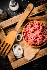 Minced meat on a wooden tray with onion rings. 