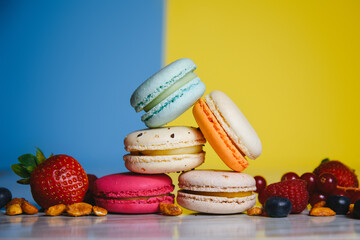 Colorful macarons. Small French cakes. Sweet and colorful french macaroons. Many tasty macarons with fresh berries, raspberries and blueberries, nuts and strawberries on a blue yellow background.