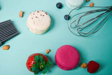 Colorful macarons. Small French cakes. Cooking, whisk, broken macarons, fruits, strawberries, raspberries and blackberries. Cooking process on a blue background, whisk, strawberries