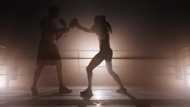 Unrecognized coach working out with female kickboxer indoors. Close-up view of a woman training her body muscles and endurance. High quality 4k footage in golden sepia bronze foggy back light
