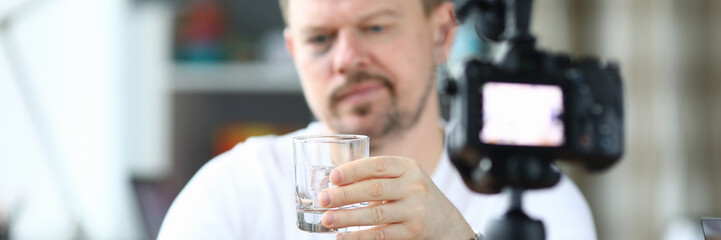 Exhausted man with black eye drinks alcohol in front of camera