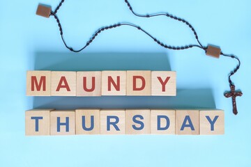 Maundy Thursday holy week concept. Wooden blocks typography with rosary flat lay in blue background.