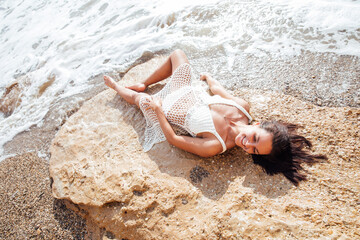 a woman in white clothes lies on a rock by the sea