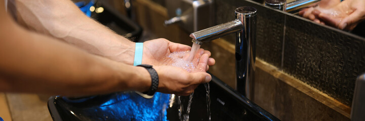 Man washes hands in the sink in bathroom at home checking temperature by touching running water with hand