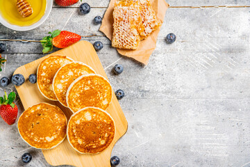 Homemade pancakes on a cutting board with honey and berries. 