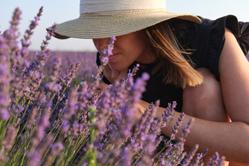 Relaxed woman enjoying the smell of lavender flowers in a field at sunset.