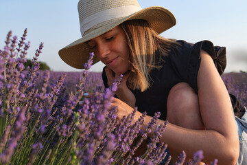 Relaxed woman enjoying the smell of lavender flowers in a field at sunset.